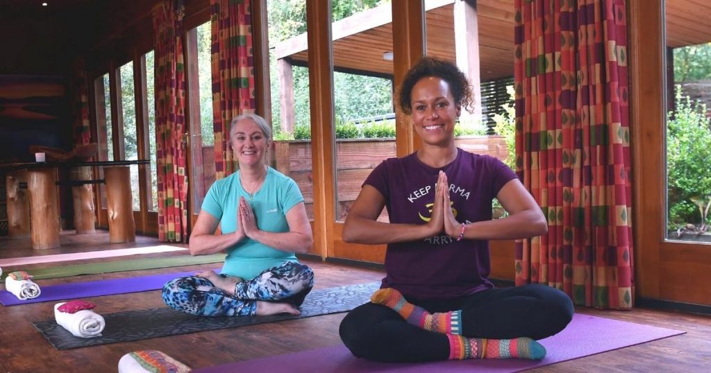 Amanda Powell (Anjali) and Anita Evans who are both Yoga teachers in South Wales sitting in easy cross-legged pose with hands in Namaskar mudra ahead of a Yoga Day Retreat in a cosy woodland chalet in Cardiff, South Wales. Picture copyright: https://www.richardwilliamsphoto.co.uk/